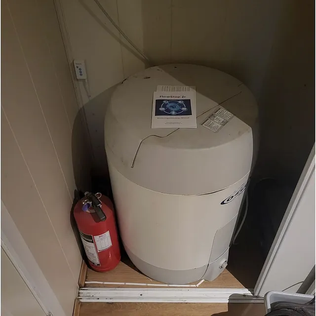 Varmtvannsbereder plassert i teknisk skap med brannslukningsapparat og installert vannstoppsystem for økt sikkerhet.